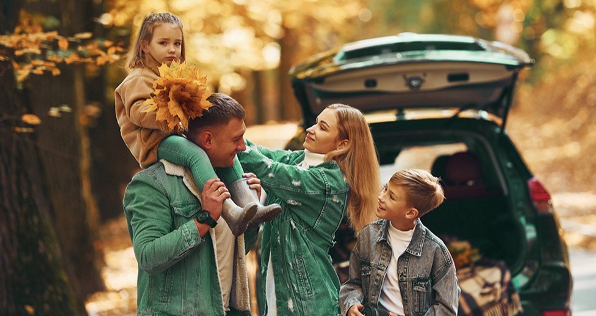 Famiglia in auto durante l’autunno, le foglie degli alberi sono gialle
