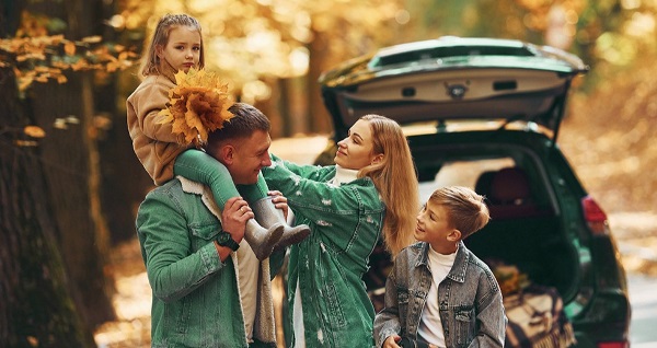 Famiglia in auto durante l’autunno, le foglie degli alberi sono gialle