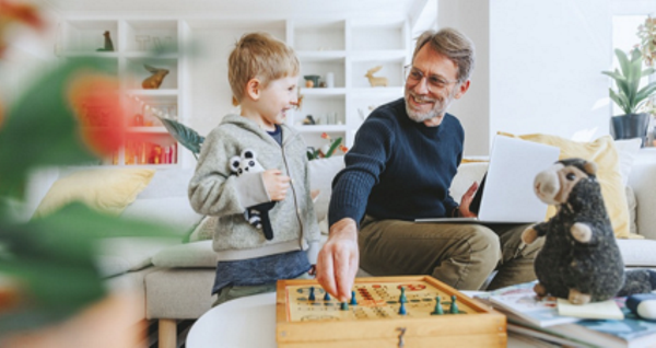 Un grand-père et son petit-fils partageant un moment joyeux en jouant à un jeu de société dans un salon cosy, entourés de jouets en peluche.