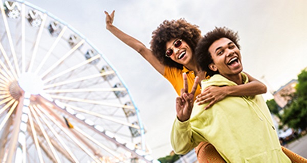 Zwei fröhliche Freunde machen Friedenszeichen mit ihren Fingern vor einem beleuchteten Riesenrad