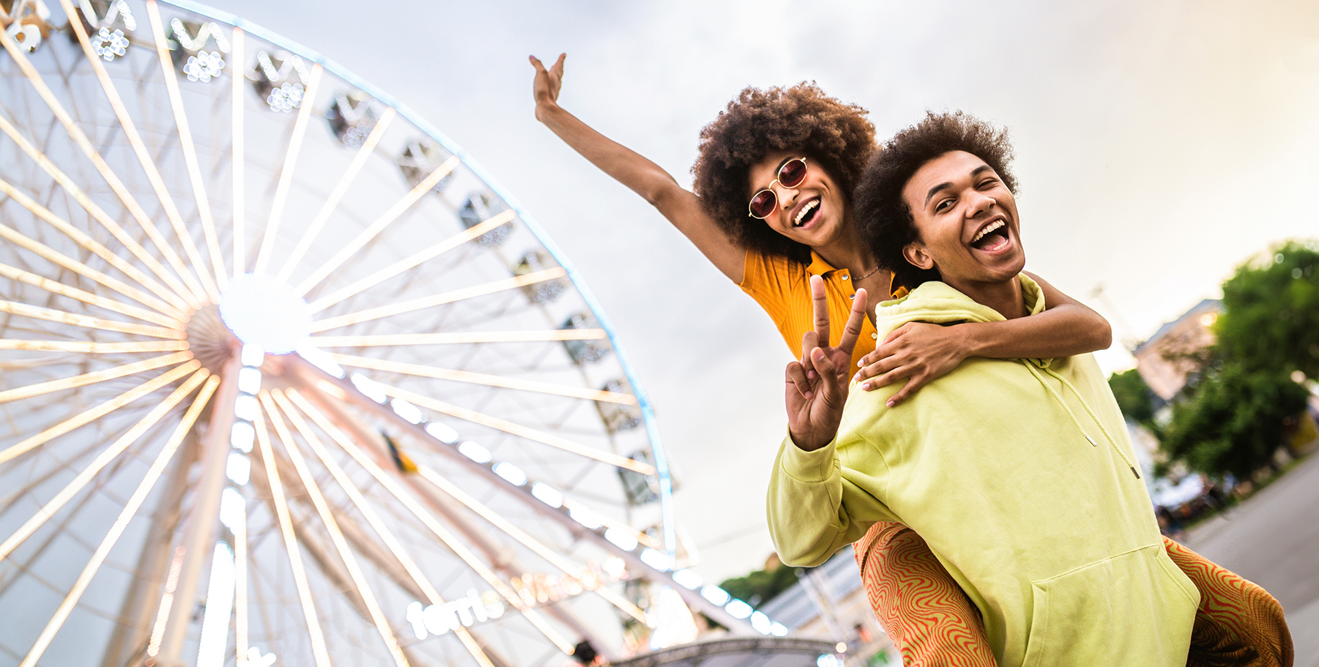 Deux jeunes adultes sourient devant une grande roue lumineuse
