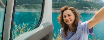 Eine Frau steht vor der Tür ihres Autos, mit einem See im Hintergrund