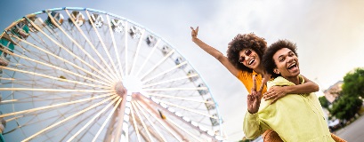 Deux jeunes adultes sourient devant une grande roue lumineuse