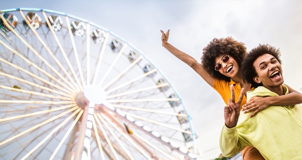 Deux jeunes adultes sourient devant une grande roue lumineuse