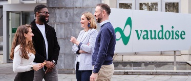 Quatre personnes discutent debout devant un bâtiment avec un logo vert et l’inscription « vaudoise ».
