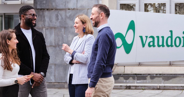 Quatre personnes discutent debout devant un bâtiment avec un logo vert et l’inscription « vaudoise ».