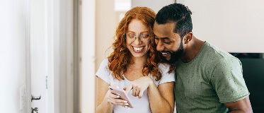 Deux personnes dans un couloir regardent un téléphone. L’une pointe l’écran, l’autre tient aussi un téléphone.