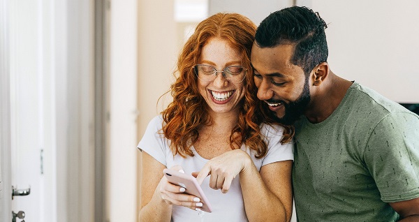 Deux personnes dans un couloir regardent un téléphone. L’une pointe l’écran, l’autre tient aussi un téléphone.