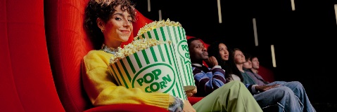 Personne au premier plan tenant deux grands seaux de pop-corn verts et blancs dans une salle de cinéma.